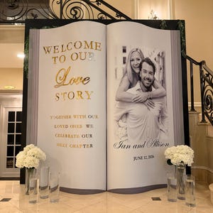 K&ouml;nnte beinhalten: Ein gro&szlig;er, buchf&ouml;rmiger Veranstaltungs-Hintergrund mit dem goldenen Text WELCOME TO OUR Love STORY, TOGETHER WITH OUR LOVED ONES WE CELEBRATE OUR NEXT CHAPTER, einem Schwarz-Wei&szlig;-Foto eines Paares und dem Text Ian and Allison JUNE 12, 2026.