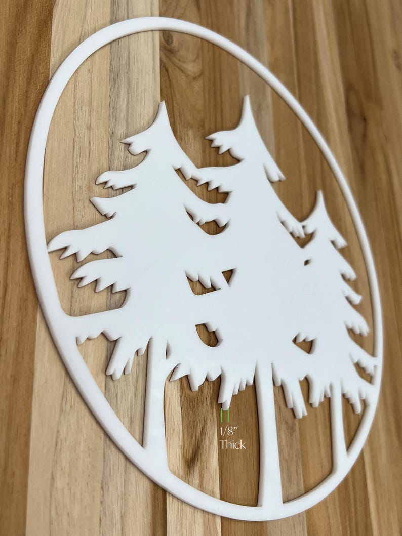 K&ouml;nnte beinhalten: Eine wei&szlig;e, kreisf&ouml;rmige Wanddekoration mit einem Ausschnittdesign aus drei Kiefern. Das St&uuml;ck ist von einem d&uuml;nnen wei&szlig;en Rand umrahmt und 0,32 cm dick. Das Design besteht aus klaren Linien und scharfen Kanten, die eine Waldsilhouette bilden.