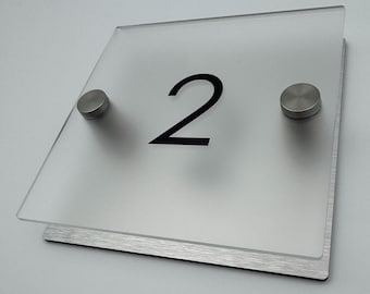May include: A frosted glass house number sign with the number "2" printed in black. The sign is mounted on a brushed silver metal base with two silver screws.