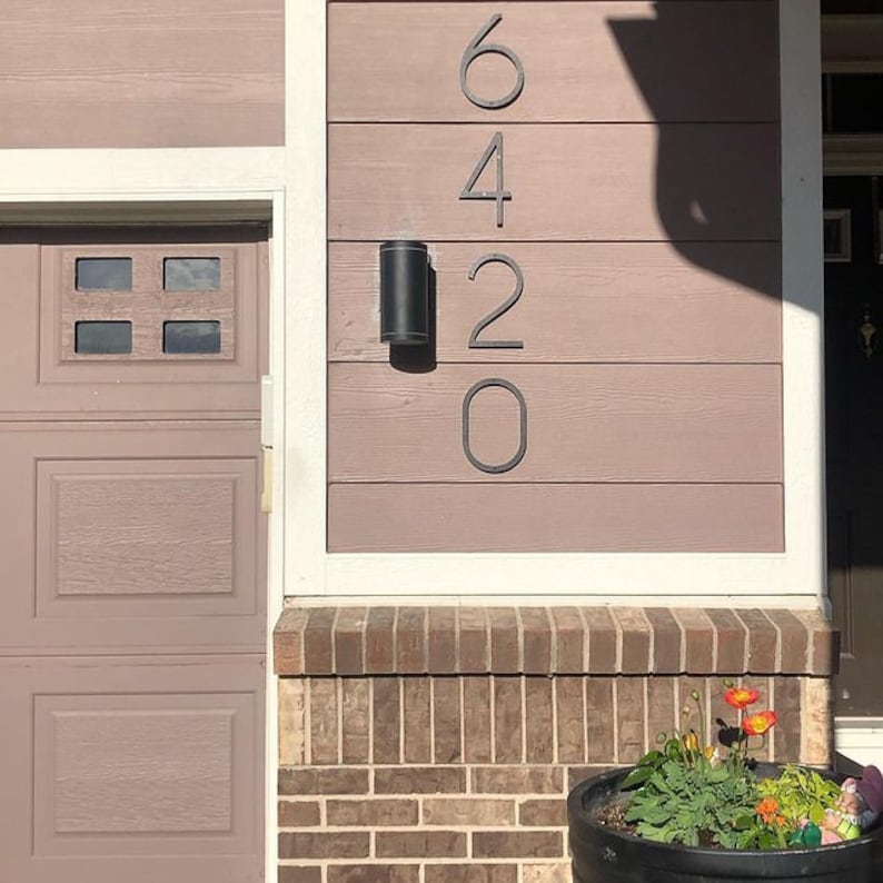 May include: A close-up of a house with a brick facade and a garage door. The house number, 6420, is displayed in black metal numbers on the side of the house.