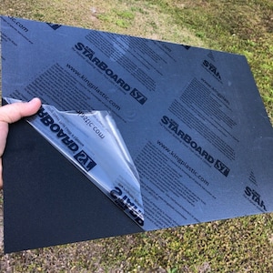 May include: A black sheet of Starboard  SY  plastic material with a protective film being peeled off. The film has the text "Starboard SY" and "www.kingplastic.com" printed on it.