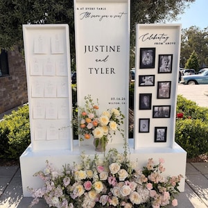 Puede incluir: Un expositor de boda de madera blanca con tres paneles verticales. El panel central dice "& AT EVERY TABLE I'll save you a seat JUSTINE and TYLER 05.16.26 WILTON, CA". El panel izquierdo contiene tarjetas de asiento y el derecho fotos.