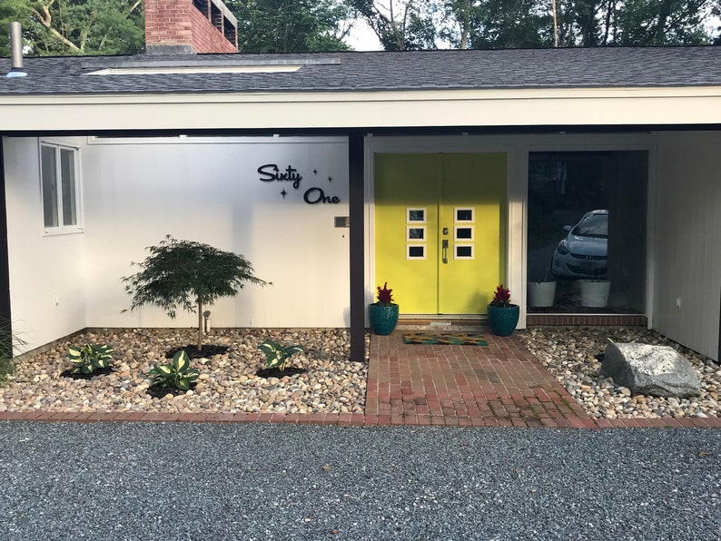 May include: A modern home with a yellow double door and a white exterior. The house number is "Sixty-One" in black lettering. The front yard has a small tree and a brick walkway.