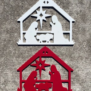May include: Two wooden Christmas nativity scene ornaments, one white and one red. Both ornaments feature a star, a manger, and figures of Mary, Joseph, and the baby Jesus.