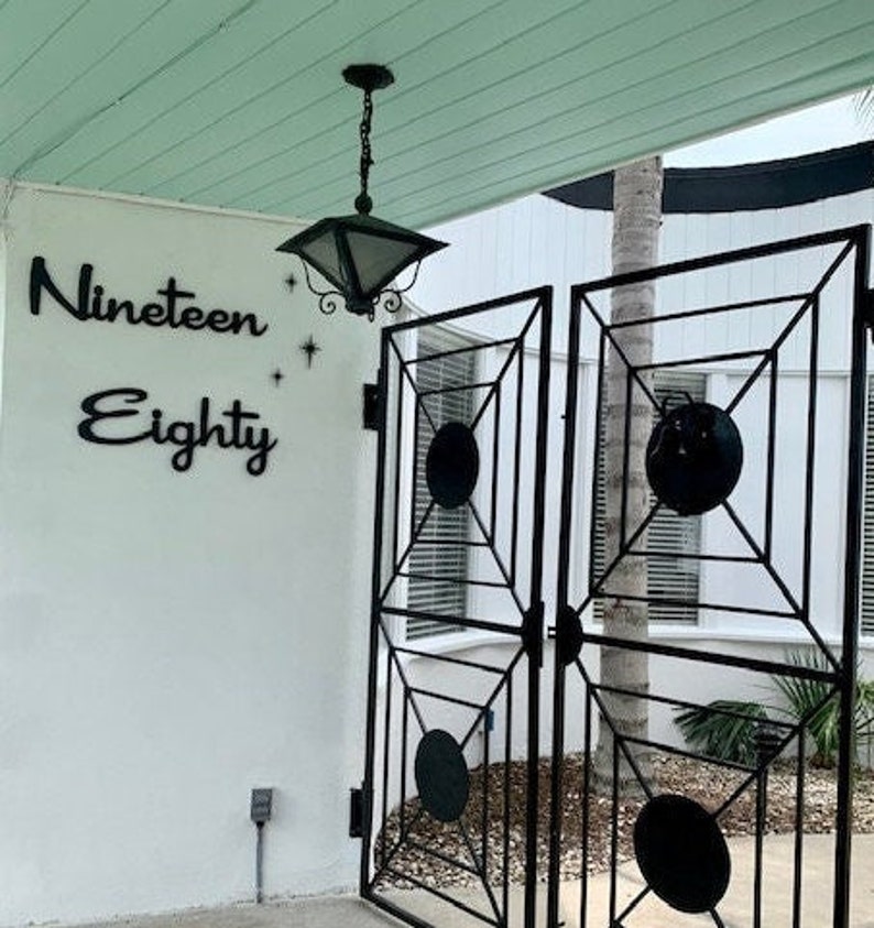 May include: A black metal gate with a white background and the words "Nineteen Eighty" on the wall behind it.