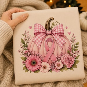 Op de afbeelding: Een vierkant gebroken wit stoffen item met een centrale illustratie van een lichtroze pompoen versierd met een grote roze en witte gingham strik, een roze bewustzijnslint en een omlijsting van roze bloemen, bladeren en kleine hartjes.