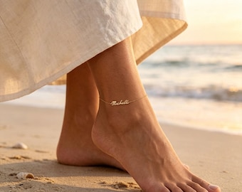 May include: A gold-toned metal anklet featuring a delicate chain and a central nameplate with the script text Michelle. The jewelry piece is worn around the ankle, showcasing a thin, polished link design that rests against the skin.