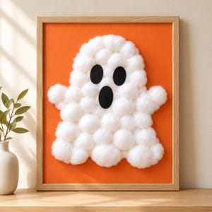 May include: A framed wall art piece featuring a ghost shape constructed from white cotton balls on a solid orange background. The ghost has two oval black eyes and an oval black mouth made of felt, all encased in a light wood frame.