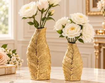 Pode incluir: Dois vasos dourados com um padrão texturizado de nervuras de folha, cada um contendo um buquê de rosas brancas. O vaso mais alto está à esquerda e o mais curto à direita. O texto LuaVaseDecor é visível no canto inferior esquerdo.