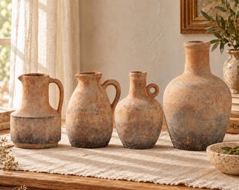 Pode incluir: Um conjunto de quatro vasos em estilo terracota com um acabamento rústico e desgastado. As peças apresentam tons terrosos de laranja e cinza carvão, com formas variadas, incluindo jarras com alças e um recipiente bojudo, alinhados.