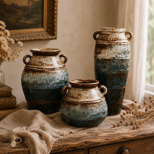 May include: A set of three ceramic vases with two handles each, featuring a reactive glaze in shades of brown, cream, and deep blue. The vases have a speckled, textured finish with a gradient color transition from the rim to the base.
