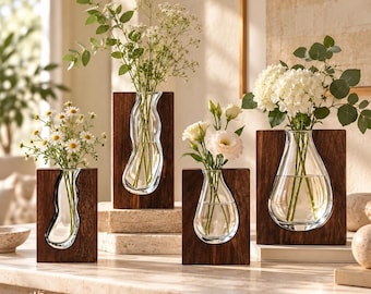 Pode incluir: Quatro vasos de vidro transparente inseridos em blocos de madeira castanho-escuro de alturas variadas. Cada vaso contém arranjos florais diferentes, incluindo margaridas brancas, gipsófila e hortênsias. O texto LuaVaseDecor aparece no canto inferior.