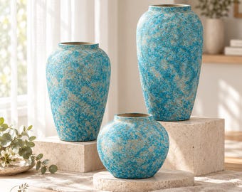 Pode incluir: Três vasos com acabamento texturizado e salpicado em tons de turquesa brilhante e bege areia. O conjunto inclui dois vasos altos de gargalo estreito e um vaso mais curto e arredondado, todos com uma aparência salpicada e desgastada.