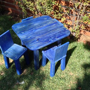 May include: A small wooden table and two matching chairs, all finished in a vibrant blue stain that highlights the natural wood grain. The set features a square tabletop with rounded corners and sturdy legs, designed for seating.