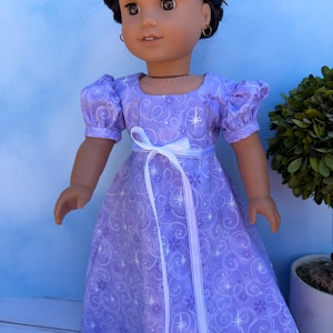 May include: A doll with dark brown hair styled in a braided updo, wearing a light purple dress with a white ribbon tied at the waist. The dress features a pattern of small purple flowers, white swirls, and four-pointed starbursts on the fabric.