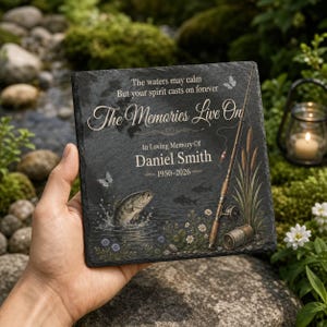 May include: A square black slate memorial plaque featuring a fishing rod, a jumping fish, and butterflies. The text reads: The waters may calm, But your spirit casts on forever, The Memories Live On, In Loving Memory of Daniel Smith, 1950-2026.