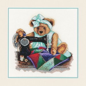 Op de afbeelding: Een bruine teddybeer met een lichtblauwe jurk en een blauwe strik zit aan een vintage naaimachine. De beer naait een kleurrijk patchwork-deken.