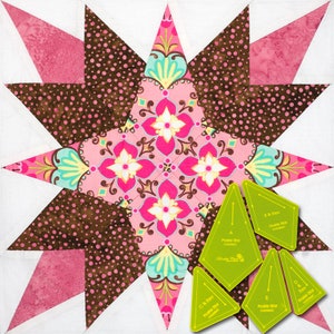 Könnte beinhalten: Nahaufnahme einer rosafarbenen und braunen Patchwork-Decke mit einem großen Sternmuster in der Mitte. Die Decke ist aus verschiedenen Stoffen gefertigt, darunter ein Blumendruck und ein Punktmuster. Die Decke ist von einem Satz von fünf grünen Kunststoff-Nählinealen umgeben, die jeweils mit den Worten "Pro-Stit" und "Star" beschriftet sind.