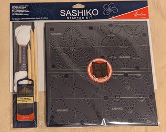 以下が含まれることがあります： Sashikoスターターキット。濃いグレーのステンシルには、花柄と幾何学模様が描かれています。 キットには刺繍糸、針、鉛筆が含まれており、「Create it！」と書かれたラベルが付いています。 パッケージには、標準的なクッションカバー48 x 48 cmを作成することも記載されています。