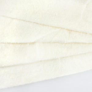 Può includere: Primo piano di una pila di tessuto di cotone bianco. Il tessuto è morbido e soffice, con una superficie leggermente strutturata.