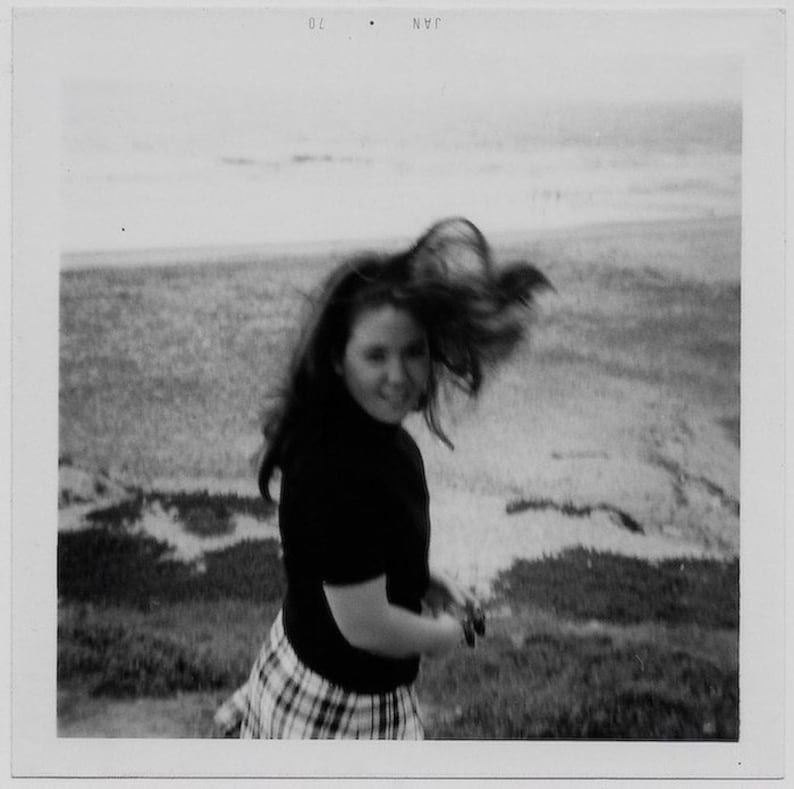 Old Photo Teen Girl wearing Black Turtleneck and Plaid Skirt Hair Blowing at the Beach Soft Focus 1970s Photograph Snapshot Vintage