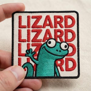 May include: A square embroidered patch with a cream-colored background and a black border. The word LIZARD is repeated in red block letters. A cartoon teal lizard with large white eyes and a black outline is waving in the foreground.
