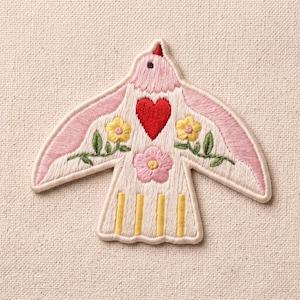 May include: An embroidered patch shaped like a bird with light pink wings, a cream-colored body, a central red heart, two yellow flowers with green leaves on the wings, a pink flower on the chest, and four vertical yellow stripes on the tail.