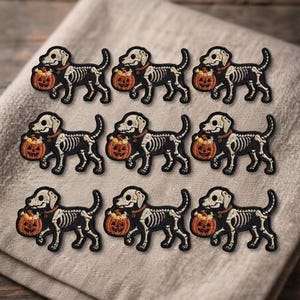 May include: Nine identical embroidered patches arranged in a grid, each depicting a dog with a visible skeleton structure. The dog is black and white, wearing a brown collar, and carrying an orange jack-o'-lantern pumpkin in its mouth.
