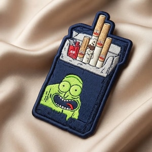 May include: A rectangular embroidered patch featuring a dark blue pack of cigarettes. The pack contains four tan cigarettes and a small red lighter, each with a cartoon face. A large, bright green cartoon character head is embroidered on the front.