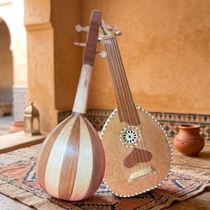 Pode incluir: Dois instrumentos de corda de madeira encostados um no outro. O instrumento da esquerda tem um corpo arredondado com faixas de madeira clara e escura. O instrumento da direita apresenta um tampo plano com uma roseta circular e um detalhe em forma de coração.