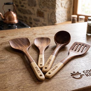 Peut inclure: Un ensemble de quatre ustensiles de cuisine en bois avec des têtes en bois brun foncé et des manches en bois plus clair. Chaque manche est gravé des caractères japonais 真木真工 et comporte un trou circulaire à l'extrémité. L'ensemble comprend une spatule pleine, une petite cuillère, une louche profonde et une spatule ajourée.