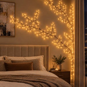 Pode incluir: Uma luminária de parede decorativa em forma de ramo de árvore com hastes finas e escuras e numerosas pequenas luzes LED de tons quentes presas aos galhos. O arranjo de luz estende-se pela parede, criando uma silhueta orgânica.