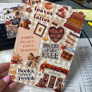 Puede incluir: Una hoja de pegatinas rectangular con un fondo de cuadros vichy beige y varias ilustraciones de temática otoñal que incluyen calabazas, una pila de libros, una taza de café, una estantería en forma de corazón, un lazo y una librería.