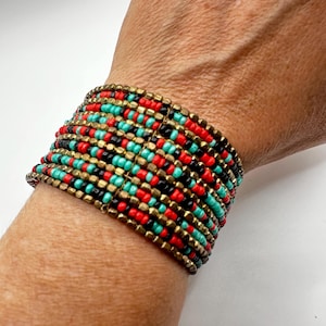 May include: A wide multi-strand bracelet featuring rows of small seed beads in alternating colors of bright red, turquoise, black, and metallic gold. The beads are arranged in a repeating pattern across several horizontal rows, creating a textured band.