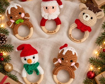 May include: Five crochet baby rattles featuring Christmas characters: a gingerbread person, Santa Claus, a reindeer, and a snowman. Each toy is attached to a smooth, round wooden ring. The wooden rings are engraved with names or holiday greetings.