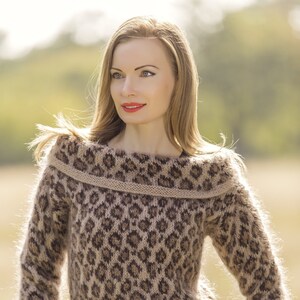 Peut inclure: Un pull à col bateau en maille douce et moelleuse à imprimé léopard brun et noir. Le pull a une coupe ample et est porté avec une jupe noire et une ceinture noire. Le texte "SuperTanya® Hand crafted knitwear" est visible en bas de l'image.