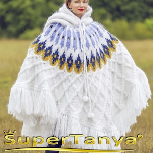 May include: A white hooded poncho with a geometric pattern in blue and gold. The poncho has a fringe trim and a drawstring. The text "SuperTanya" and "Hand crafted knitwear" are visible at the bottom of the image.