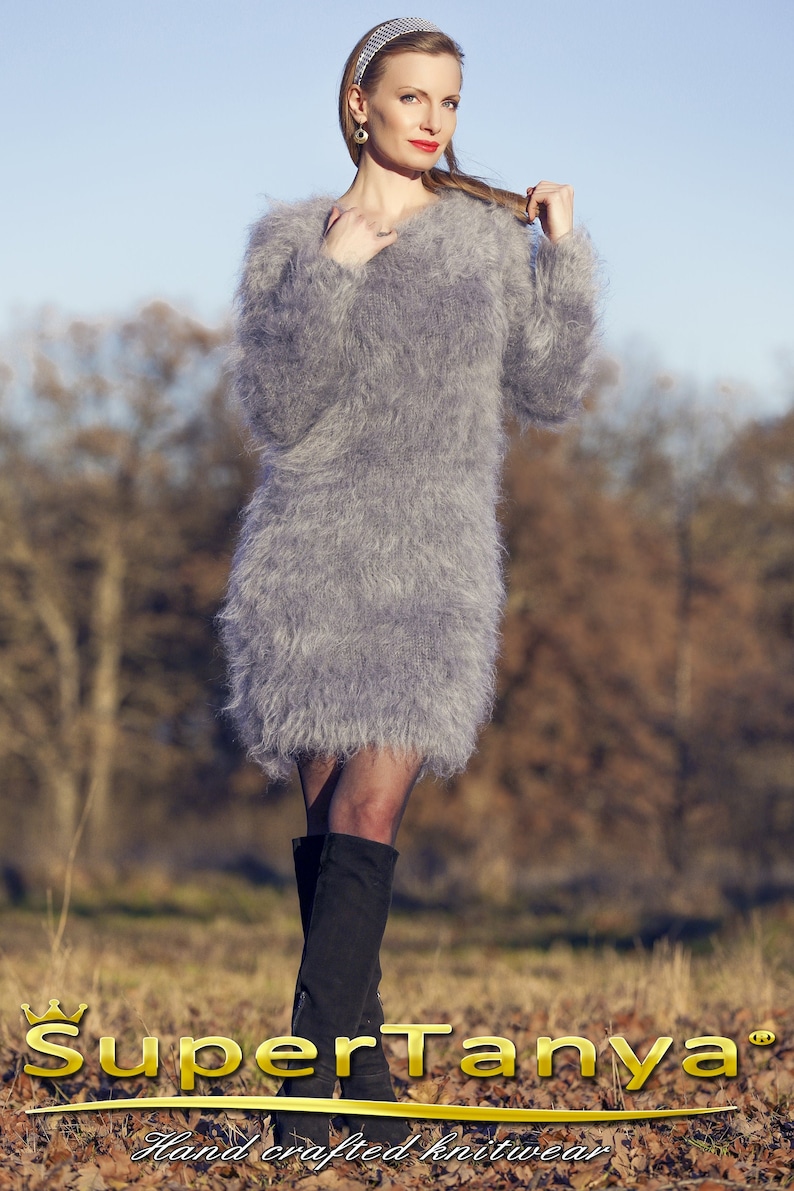 May include: A woman wearing a gray, fuzzy, long-sleeved dress and black boots. The dress has a V-neck and a soft, textured appearance. The image includes the text "SuperTanya" and "Hand crafted knitwear".