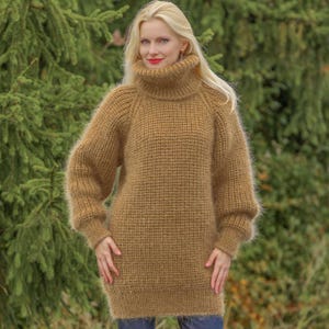 Peut inclure: Un pull-over marron à manches longues et surdimensionné avec un col roulé haut. Le pull a un aspect texturé et tissé et une coupe décontractée. Les manches sont longues et légèrement évasées. Le modèle porte un jean bleu.