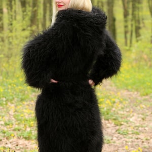 May include: A black fuzzy knit cardigan with a hood. The cardigan is long and has a belt. The model is wearing the cardigan in a forest setting.