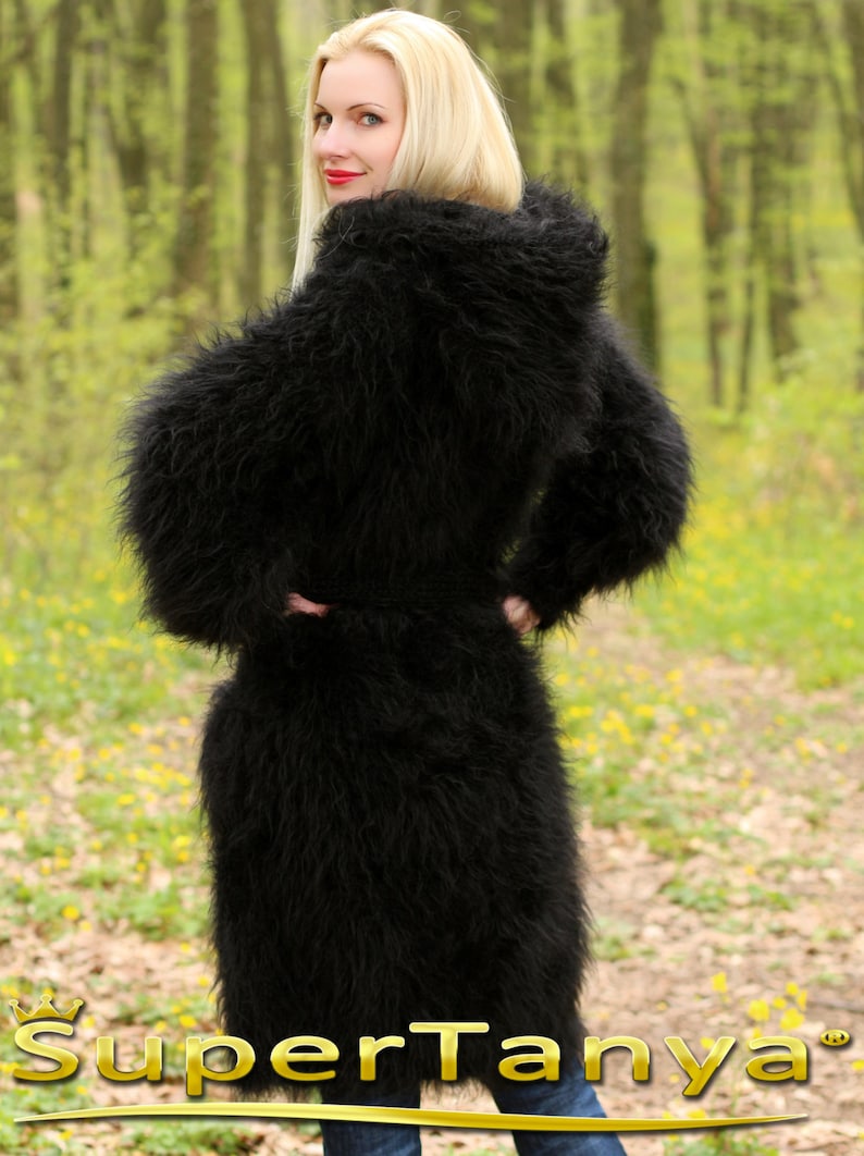 May include: A black fuzzy knit cardigan with a hood. The cardigan is long and has a belt. The model is wearing the cardigan in a forest setting.