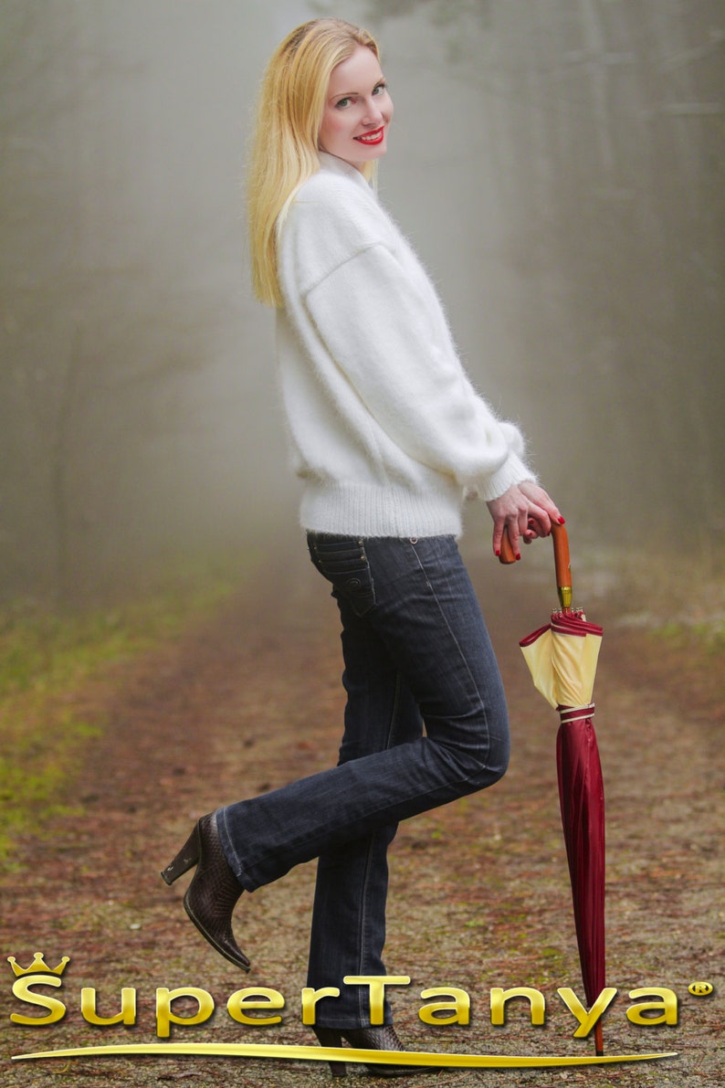 May include: A woman in a white fuzzy sweater and blue jeans is holding a red and yellow umbrella. She is standing on a path in a foggy forest.