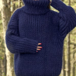 May include: A navy blue oversized hand-knitted turtleneck sweater with a thick, fuzzy texture. The sweater is made by SuperTanya, a hand-crafted knitwear brand.