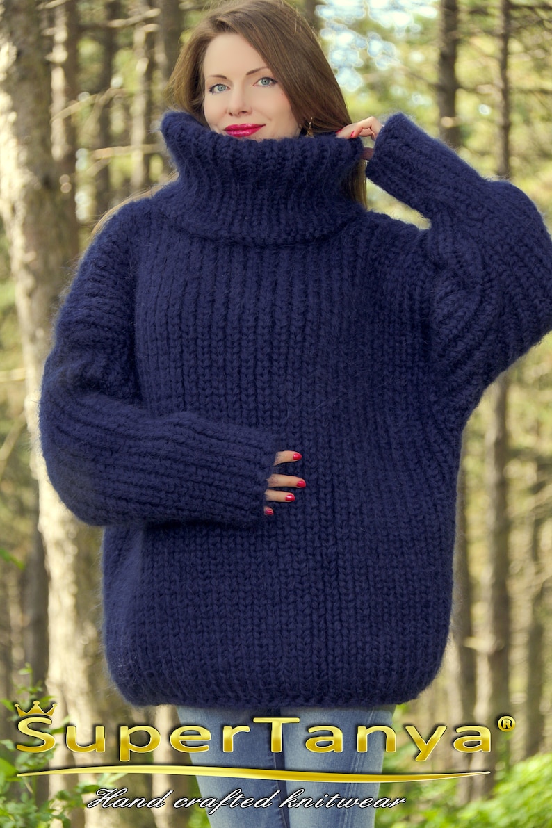 May include: A navy blue oversized hand-knitted turtleneck sweater with a thick, fuzzy texture. The sweater is made by SuperTanya, a hand-crafted knitwear brand.