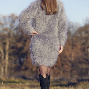 May include: A gray, fuzzy, long-sleeved dress with a mini skirt. The dress is worn with black boots. The image includes the text "SuperTanya" and "Hand crafted knitwear" in gold lettering.