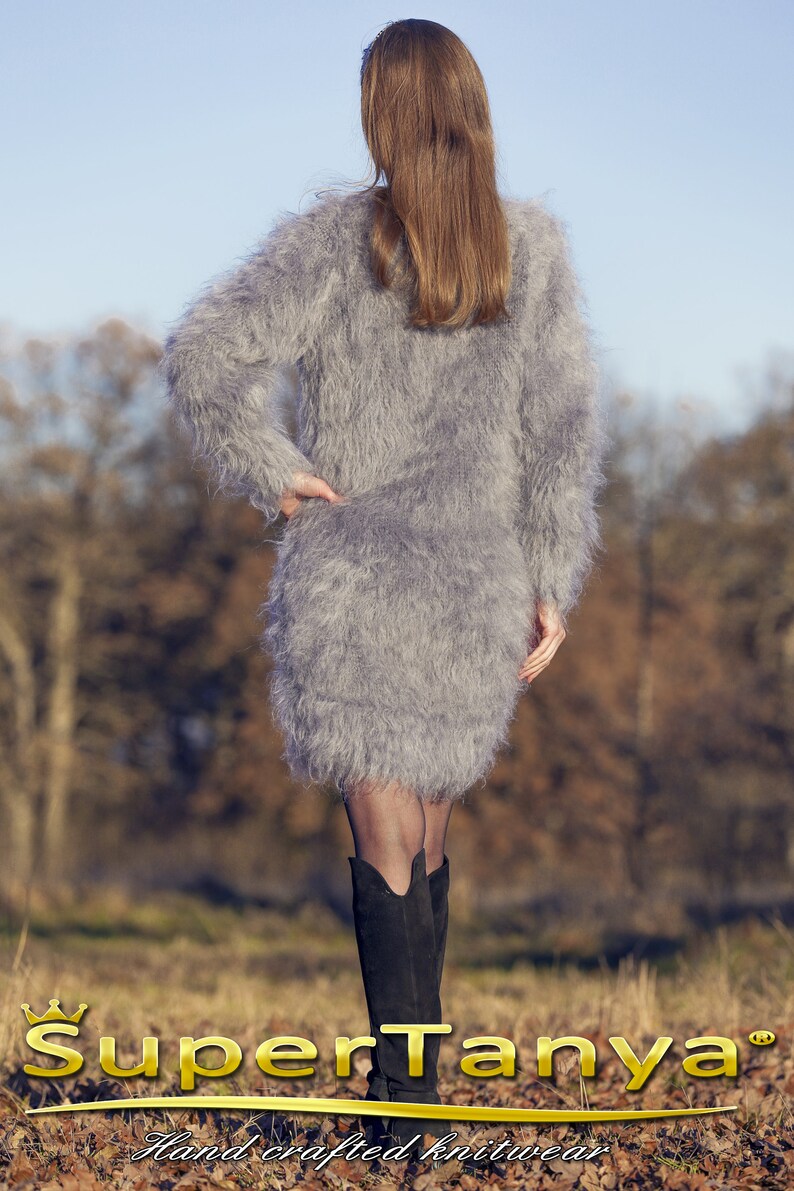 May include: A gray, fuzzy, long-sleeved dress with a mini skirt. The dress is worn with black boots. The image includes the text "SuperTanya" and "Hand crafted knitwear" in gold lettering.