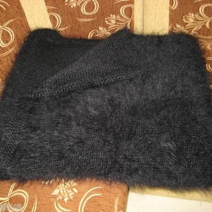 May include: A black fuzzy knit scarf or shawl. The scarf is folded in half and laid on a patterned fabric surface.
