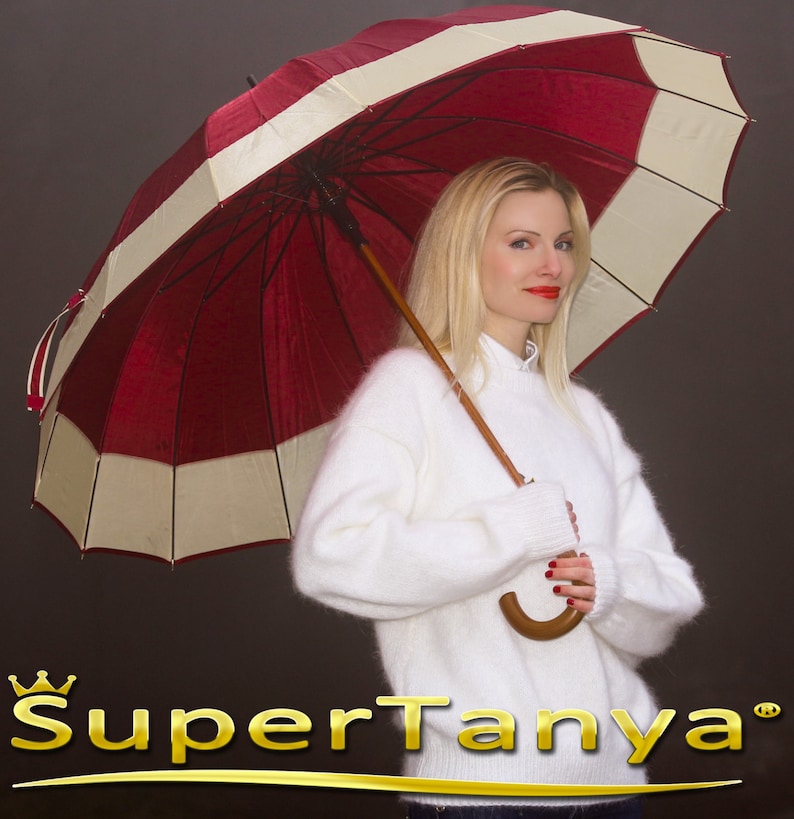 May include: A woman wearing a white fuzzy sweater holds a red and white striped umbrella. The umbrella has a wooden handle. The background is a dark gray.