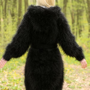 May include: A long, black, fuzzy mohair cardigan with a hood and a belt. The cardigan is worn by a person standing in a forest.