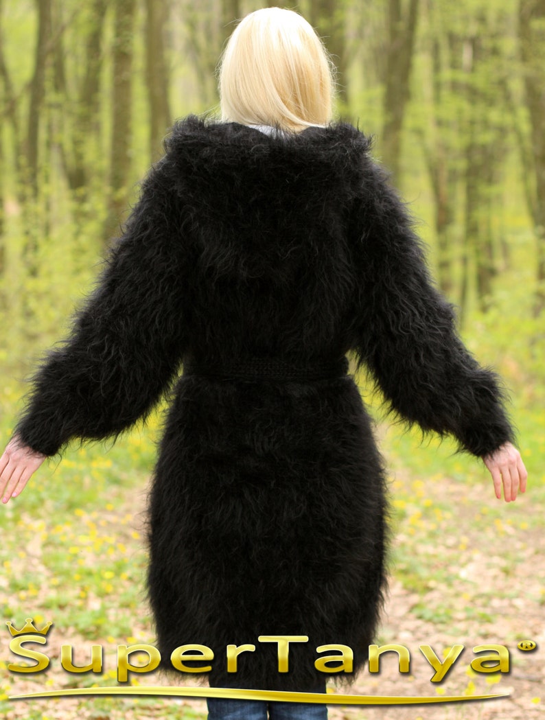 May include: A long, black, fuzzy mohair cardigan with a hood and a belt. The cardigan is worn by a person standing in a forest.